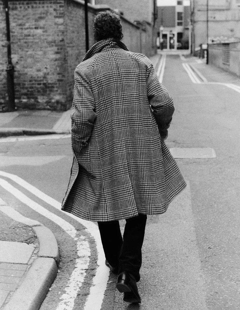 Black-and-white look book image of a man in a check coat on a street
